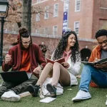 Three students sitting outdoors on campus sharing notes